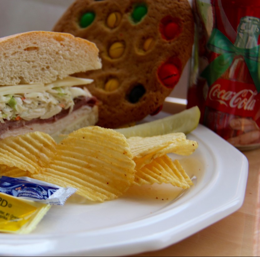 Sandwich and a pickle spear, Soda, bottled water or sparkling water, Chips, Cookie